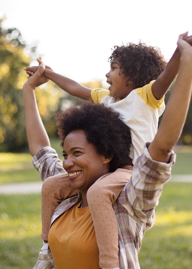 African American mother and daughter standing in park. Little girl on mother shoulders