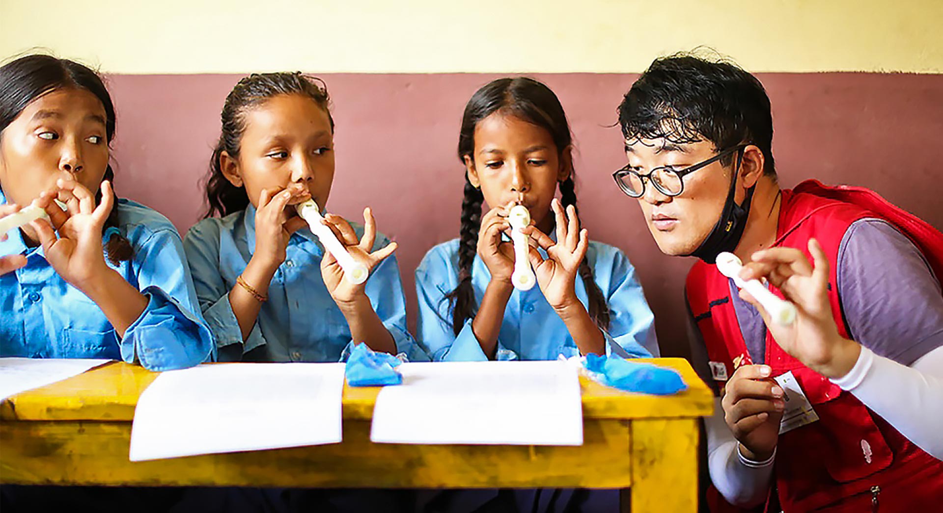 3 girls practicing the recorder and a volunteer teacher listening at Shree Seti Devi School in Nepal